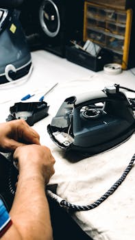 Hands working on repairing an iron in a workshop. Tools and parts are visible.